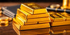 Stacked gold bars on a polished surface with coins.