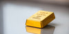 Photograph of a gleaming gold bar on reflective surface.